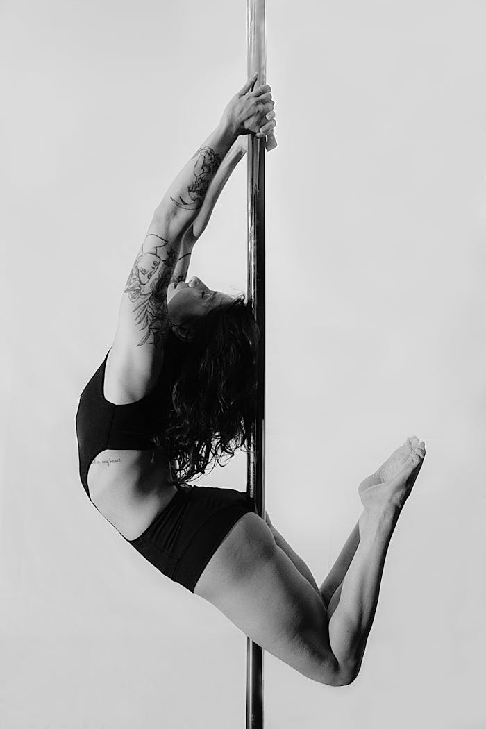 A focused female athlete performing an elegant pole dance maneuver in black and white.